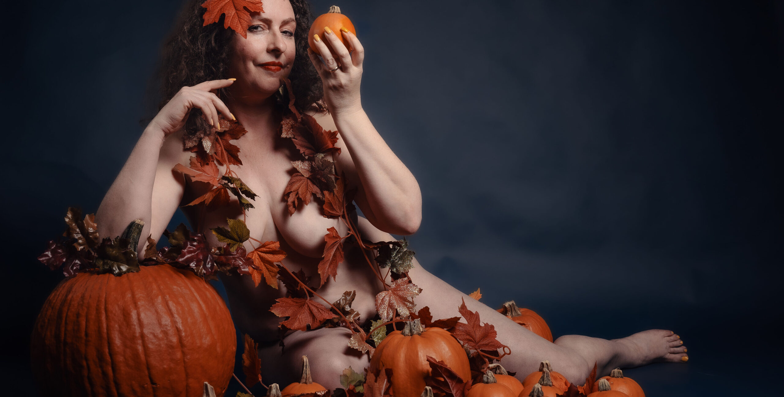 gretel, naked, wrapped in fall leaves holding a pumpkin